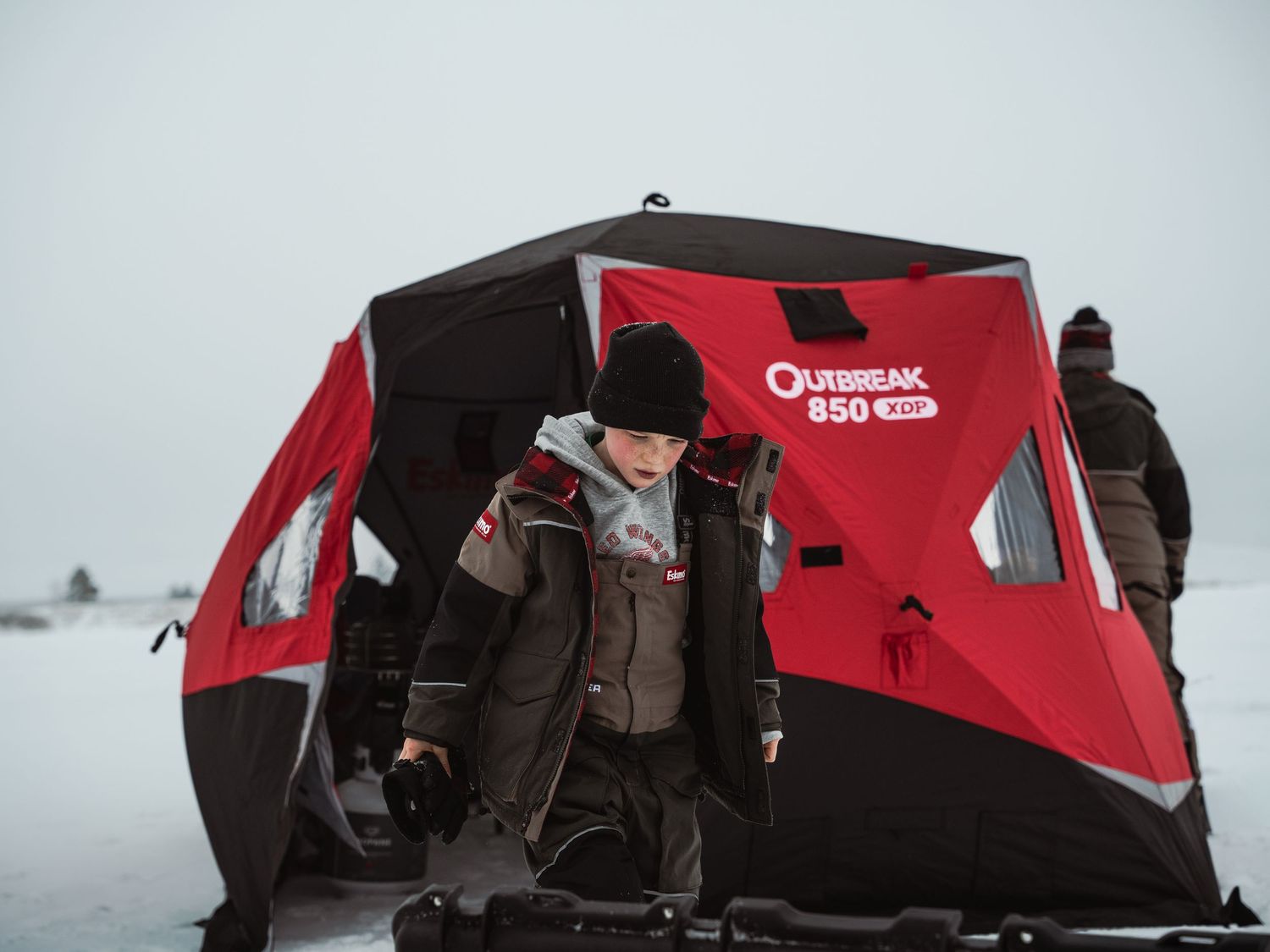 Red and black portable ice fishing shelter set up on snowy lake.
