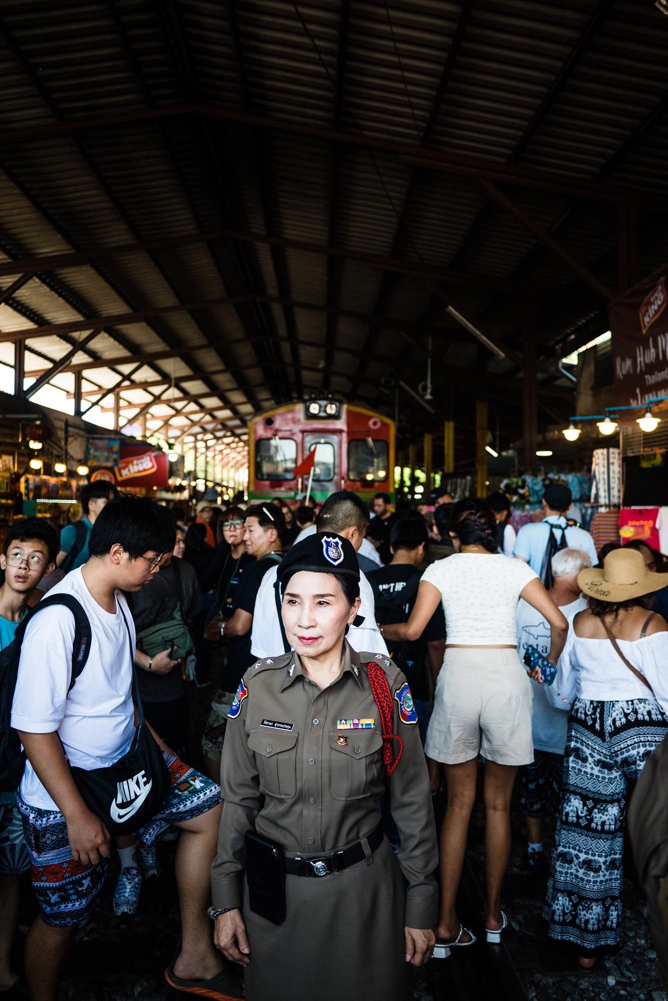 Crowded scene at a bustling train station or market in Thailand with uniformed personnel and tourists.