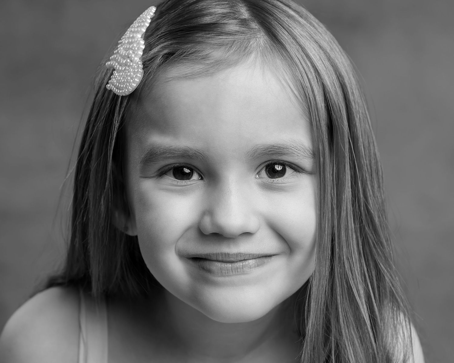 A close-up black and white portrait of a smiling young girl with a sparkly hair clip and long straight hair.