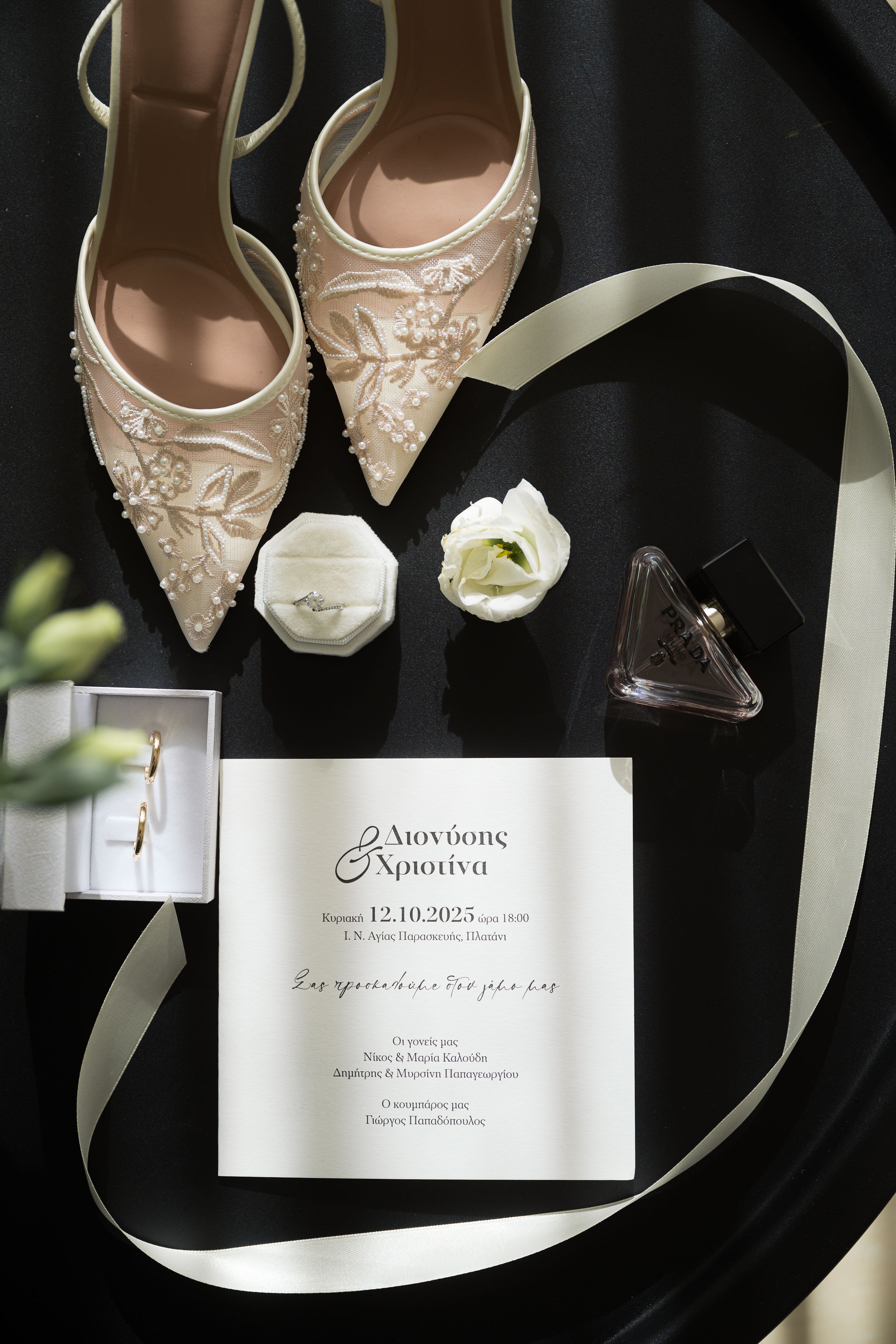 Elegant bridal shoes and wedding invitation displayed on black background with white ribbon accents.