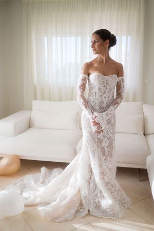 A stunning lace wedding dress displayed in an elegant white room with modern furniture.