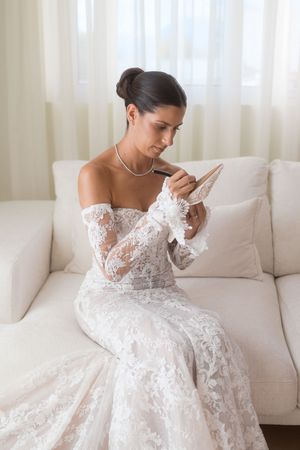 A detailed shot of an intricate lace wedding gown against white furniture and curtains.