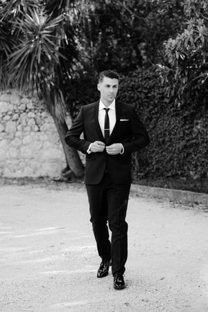 Black and white photos of groom in classic tuxedo walking and posing outdoors.