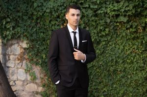 Row of groomsmen in suits posing against ivy covered wall.