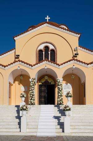 A Mediterranean-style church exterior with cream walls, arched entryway and floral wedding decorations.