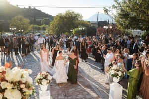Large wedding party and guests celebrate outdoors during golden hour.