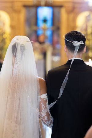 Wedding ceremony in a church with flowing white veils and formal attire visible from behind.