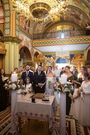 Wedding ceremony in ornately decorated Orthodox church with gilded chandelier and painted murals.