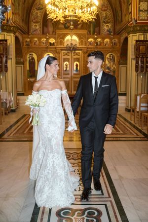 Elegant wedding couple poses in a luxurious gilded ballroom with ornate chandeliers and decorative floor patterns.