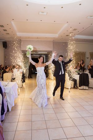 Couple performs first dance at wedding reception with sparkler effects creating magical atmosphere on white tiled floor.