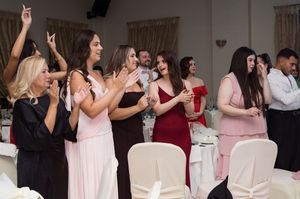 Wedding guests in pink and white attire dance and celebrate together at an indoor reception venue.