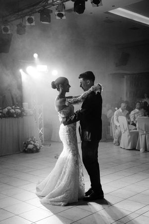 Black and white photo captures romantic first dance between newlyweds in dimly lit ballroom.