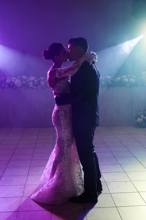 A couple shares their first dance on a tiled floor under dramatic purple and blue lighting at their wedding reception.