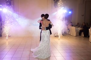 A couple dances on a white tiled ballroom floor under purple lighting with sparklers creating a magical atmosphere.