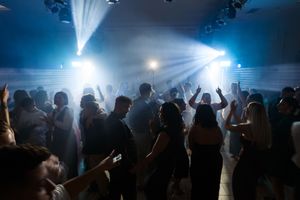 Silhouettes of concert crowd with raised arms against bright blue stage lights and fog creating atmospheric ambiance.