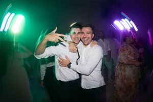 People dancing and celebrating at a party with colorful green and purple lighting effects in the background.