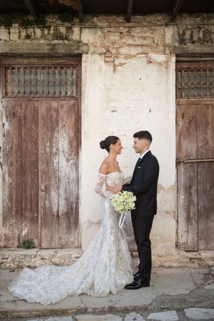 A romantic wedding photoshoot against rustic wooden doors and weathered walls.