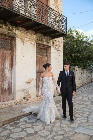 Wedding couple posing along stone walkway beside vintage building with ornate iron balcony details.
