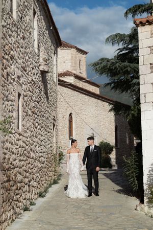 A wedding couple walks along a stone-walled pathway at a rustic Mediterranean venue on their special day.