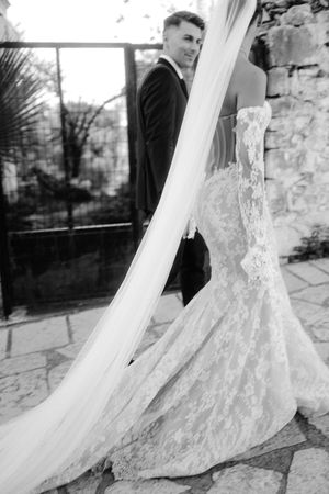 An elegant wedding dress with a flowing lace train and veil photographed in black and white.