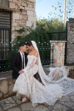 A romantic wedding photoshoot against a rustic stone wall with string lights and greenery.