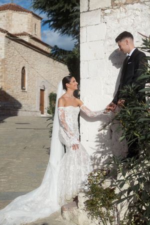 A stunning white lace wedding dress with long sleeves photographed against a rustic stone church exterior.