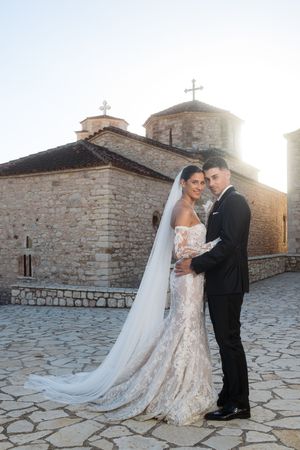 Sunset wedding portraits in front of historic stone church with dramatic lighting and flowing cathedral veil.