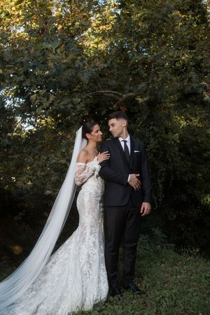 A romantic wedding couple poses outdoors in a garden setting with lush greenery and natural lighting.