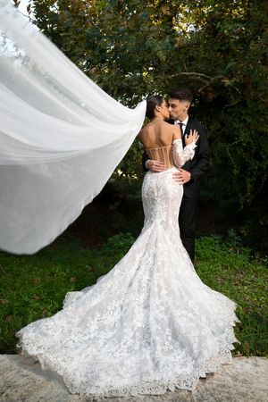 A dramatic wedding photo showing a flowing lace gown with long train and veil caught in the breeze.