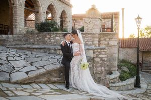 A wedding couple poses along a stone pathway during golden hour at a Mediterranean venue.