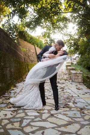 Couple performs romantic dip pose on stone patio under trees.