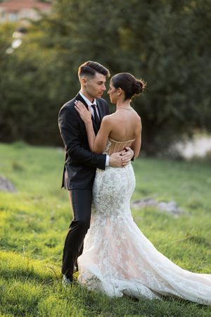 A romantic outdoor wedding portrait featuring a fitted lace gown against a natural green background.