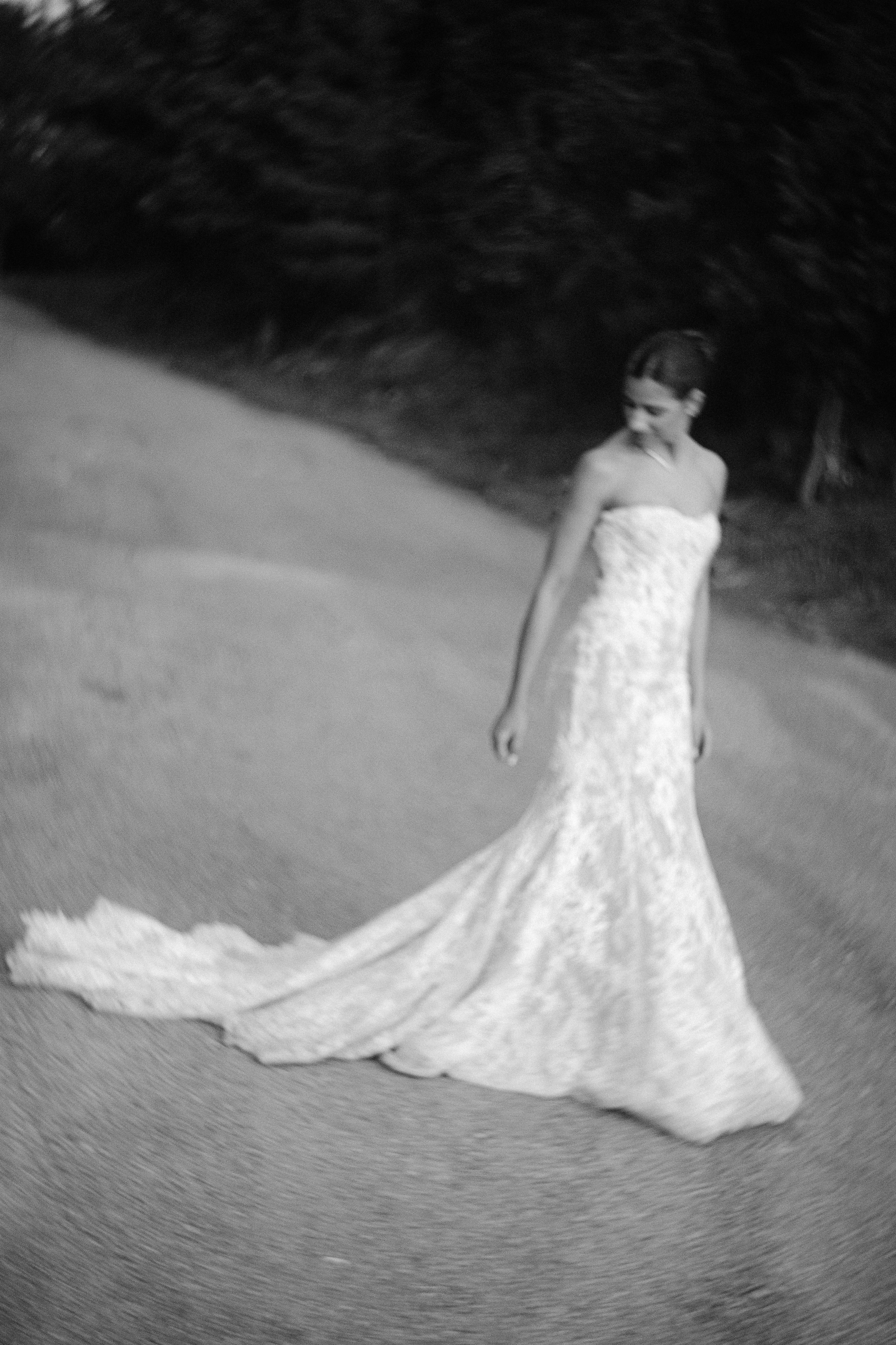 A flowing white wedding dress train photographed in black and white on a grassy surface.