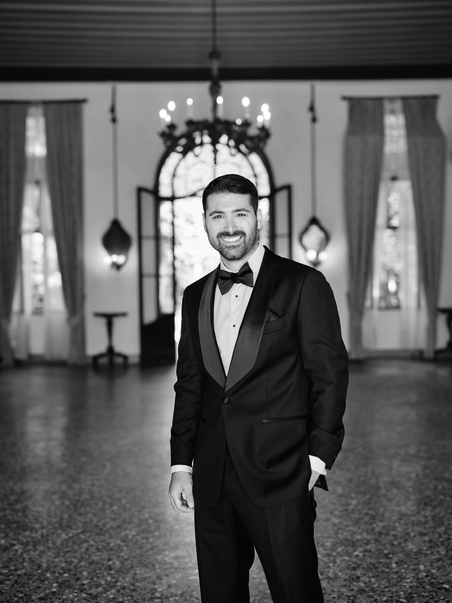 Black and white portraits of a groom in a classic tuxedo smiling in an elegant ballroom setting.