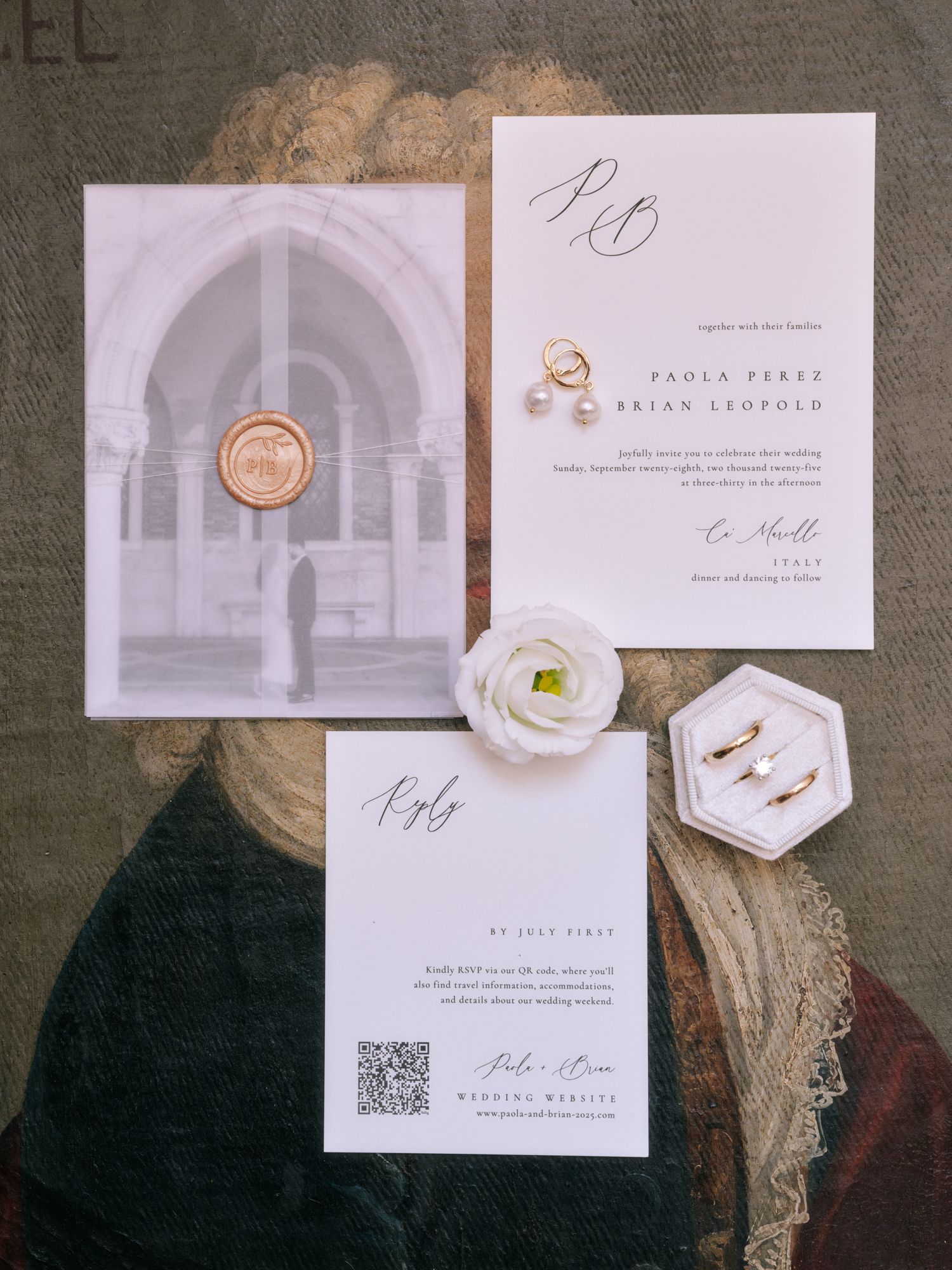 Elegant wedding invitation suite with white floral details, wax seal, and calligraphy on a vintage textured background.