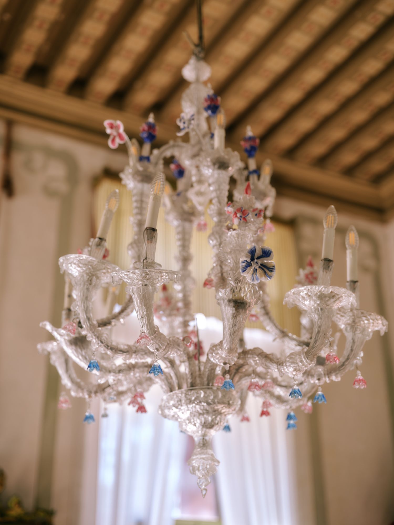 Crystal chandelier with colorful glass ornaments hangs elegantly from a wooden beam ceiling.