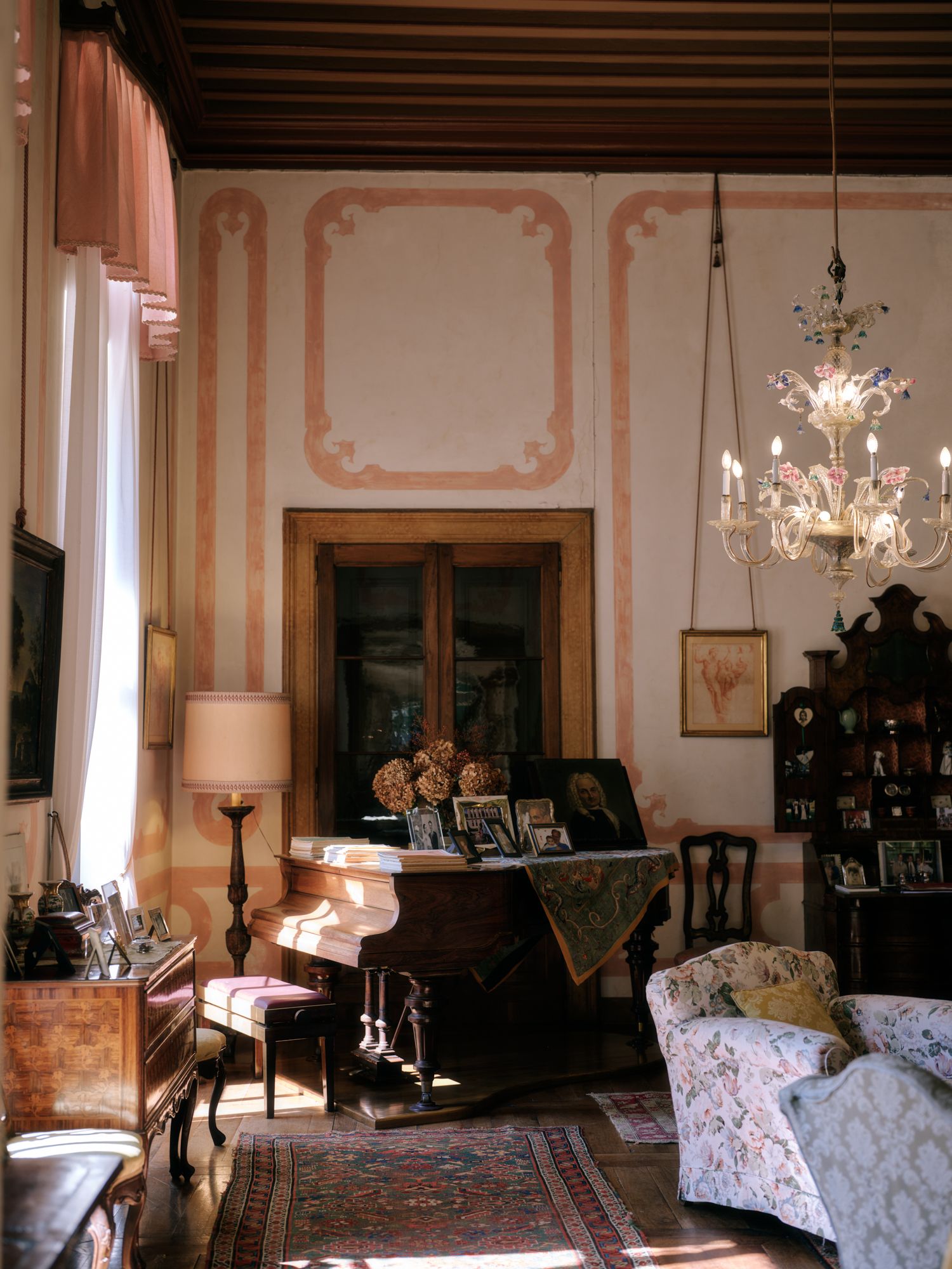 Elegant vintage living room with pink walls, crystal chandelier, piano, and antique furniture in a European-style interior.