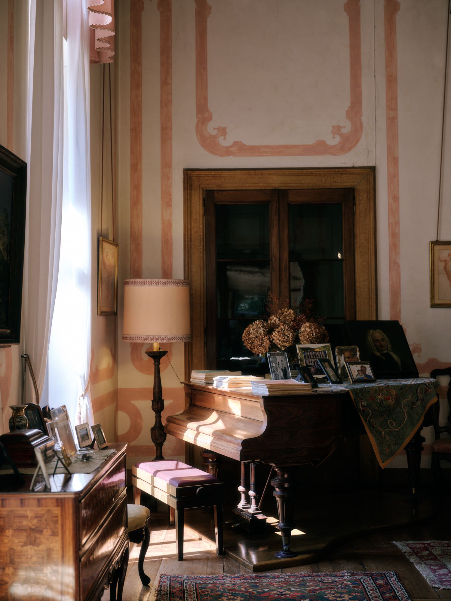 Sunlight streams through windows in an elegant Victorian-style room with decorative wall panels and antique furniture.