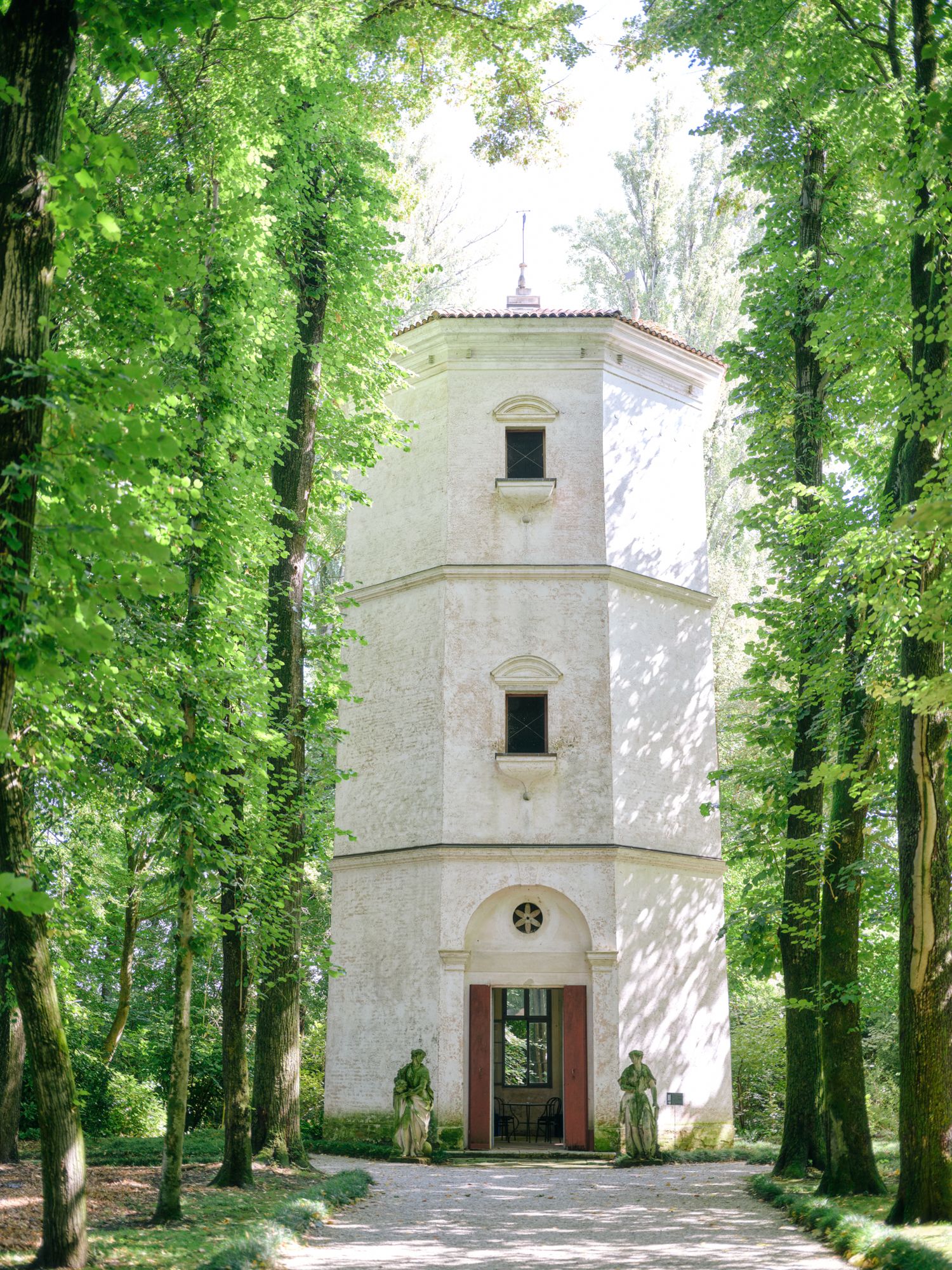 White chapel building nestled among tall green trees in a serene forest setting on a sunny day.