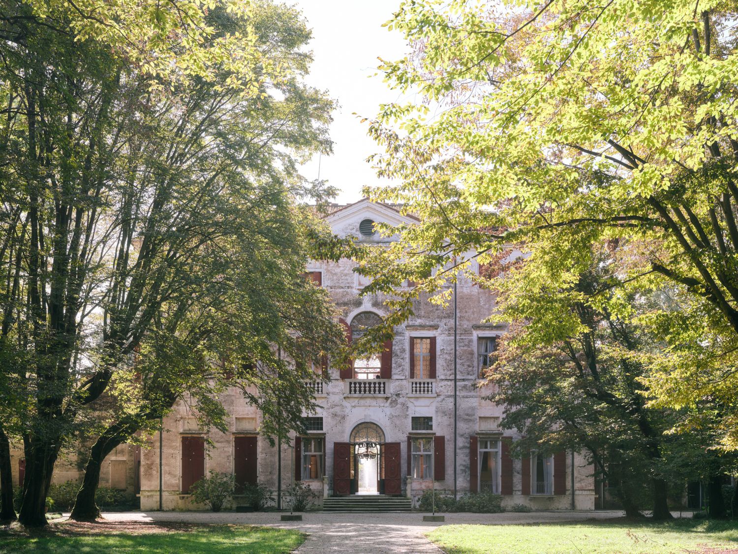 Historic brick mansion with arched entrance framed by tall green trees in a tranquil garden setting.