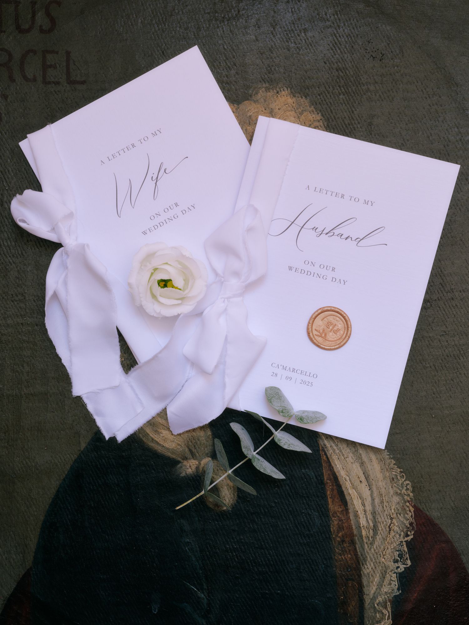 Elegant white wedding invitation cards with delicate rose and wax seal displayed on dark vintage background.