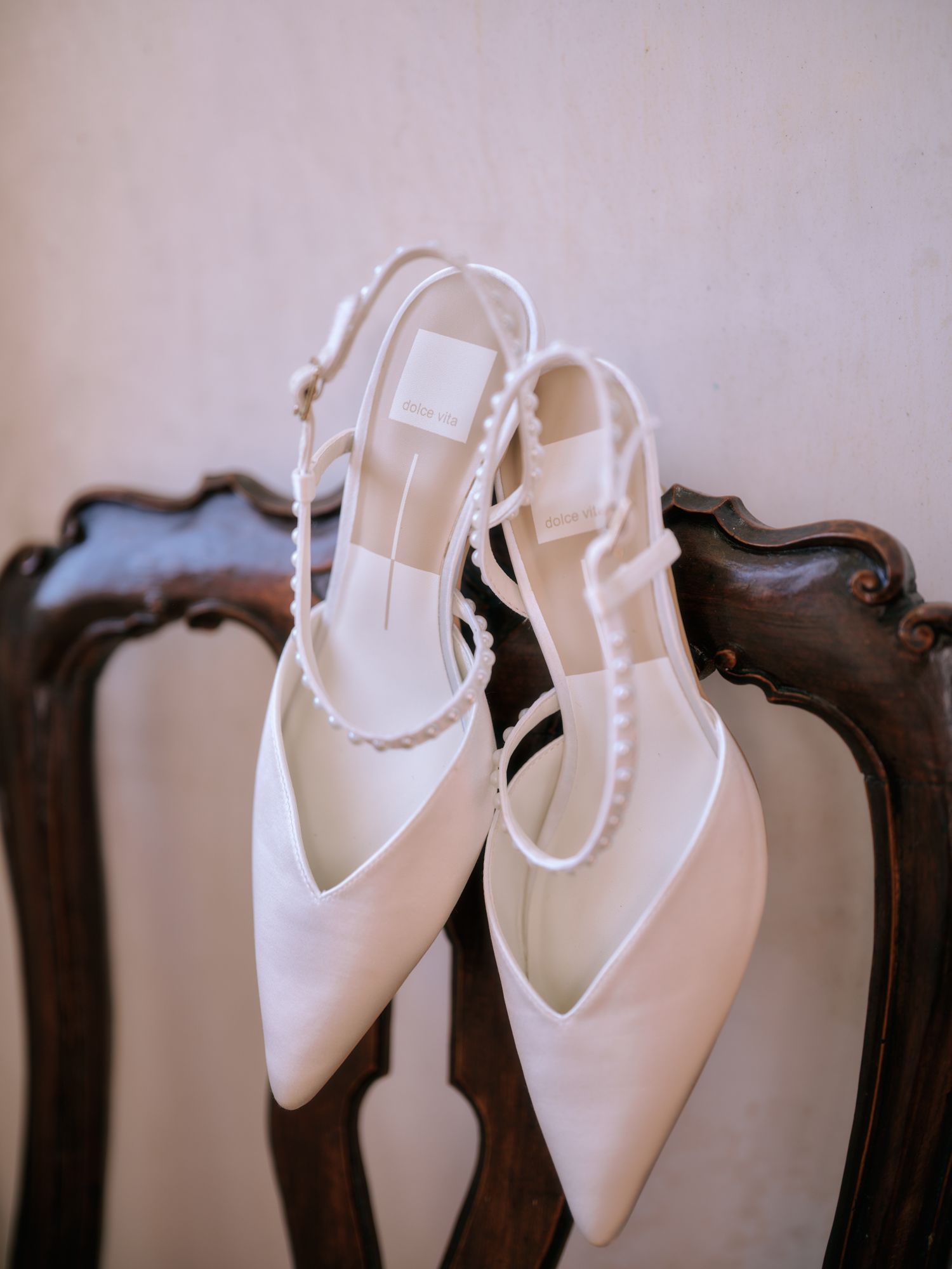 White bridal or formal shoes with ankle straps displayed on dark wooden furniture in a row.