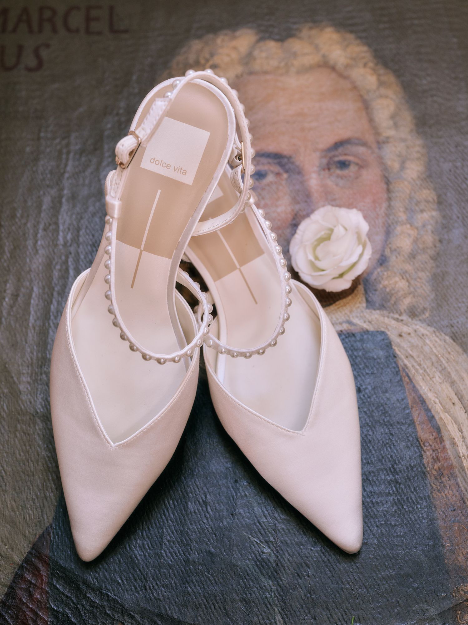 Elegant pointed-toe slingback flats in pale pink with delicate ankle straps shown from multiple angles on grey surface.