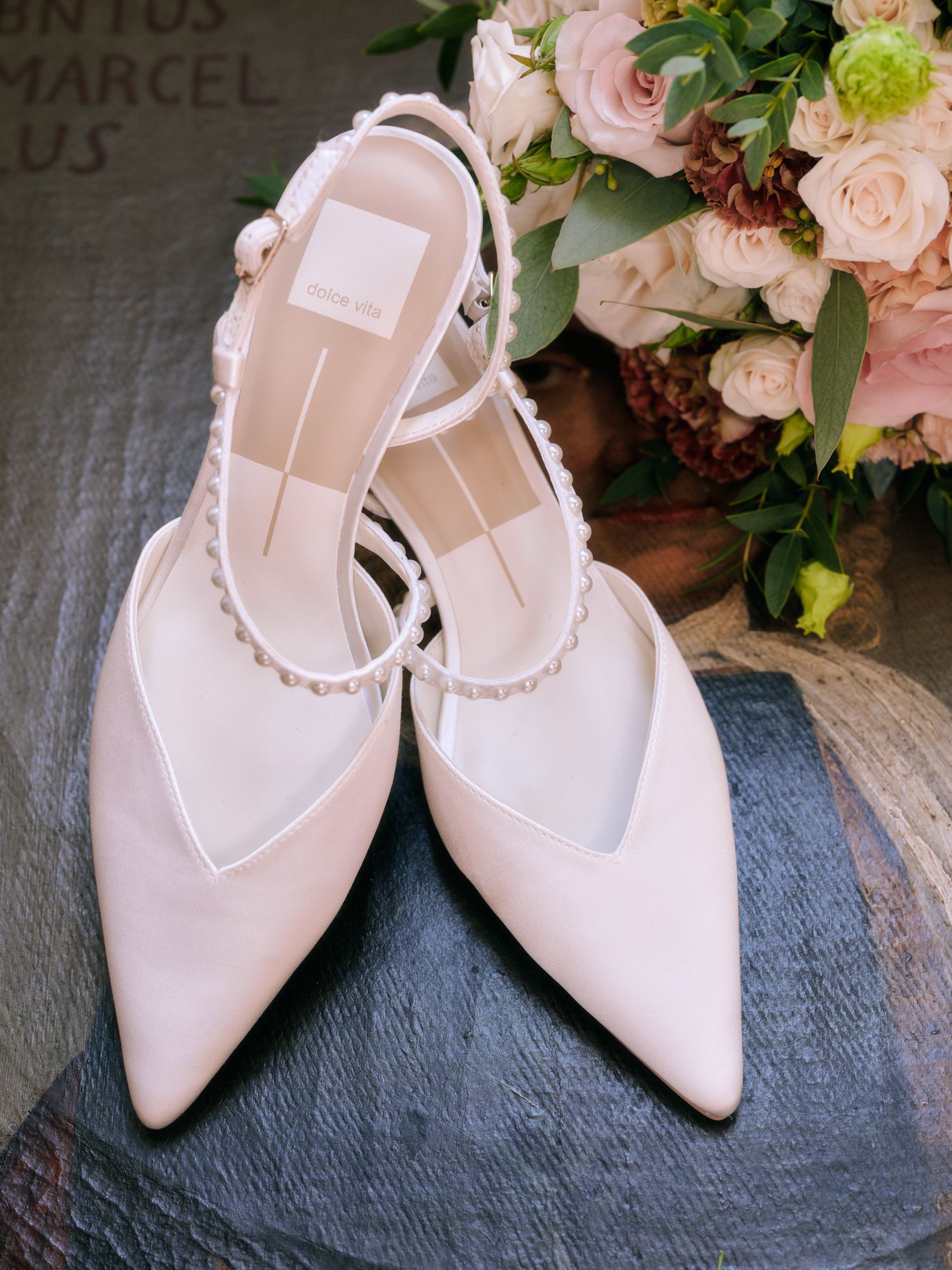 Elegant blush pink pointed-toe slingback heels with pearl embellishments displayed against a dark textured surface.