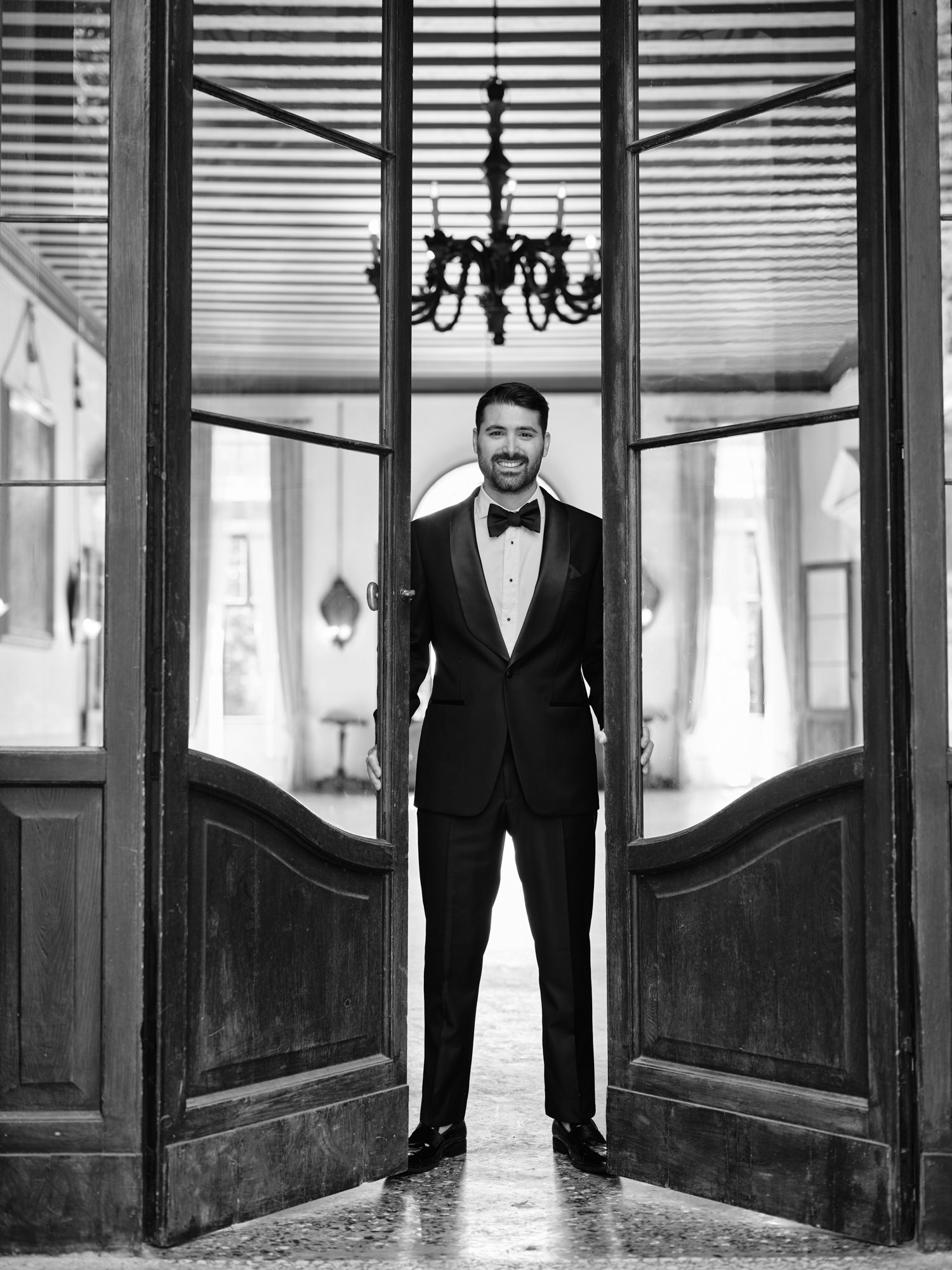 A black and white panoramic triptych showing a person in a suit standing in an elegant hallway with chandeliers.