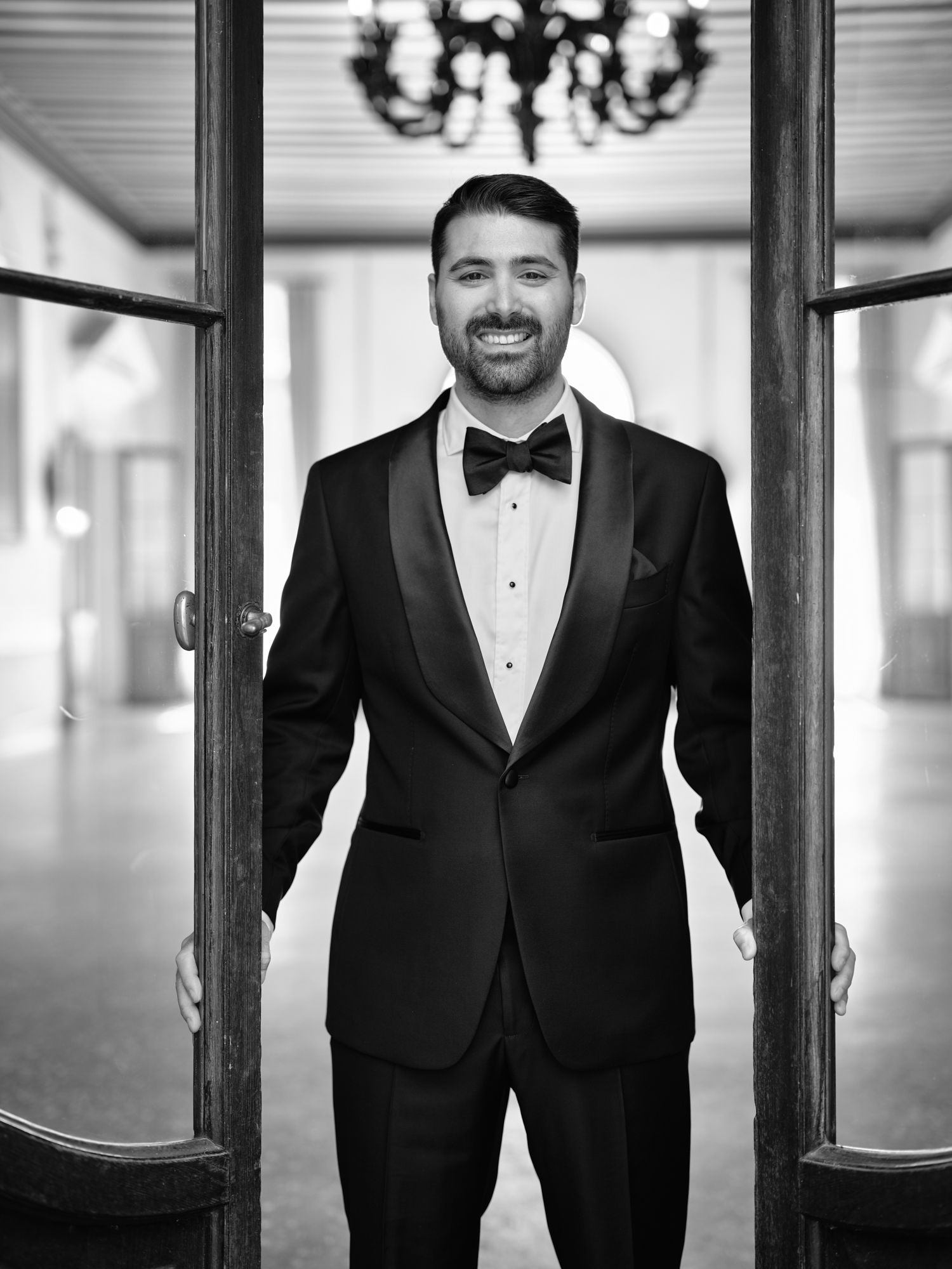 A groom in a classic black tuxedo and bow tie smiles in a series of black and white portraits.