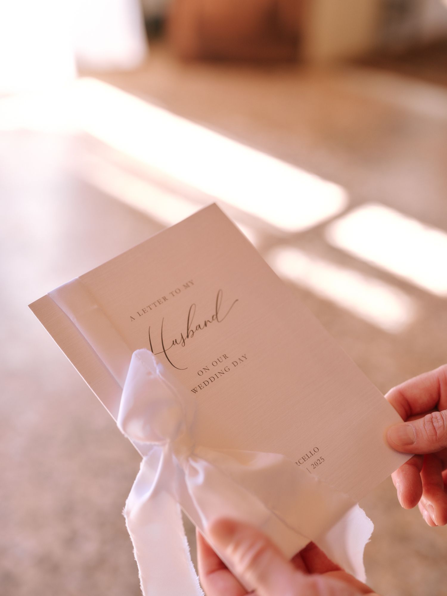 Hands holding elegant white wedding invitation cards in soft natural lighting.