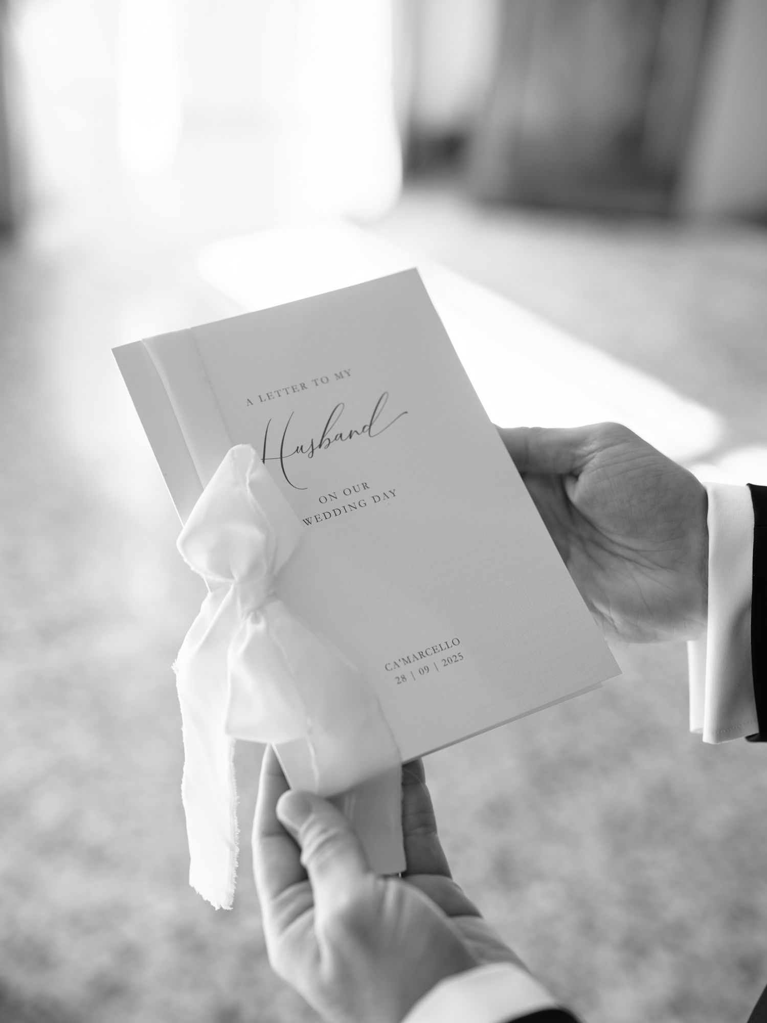 Black and white photo of hands holding a formal wedding invitation with elegant script text.