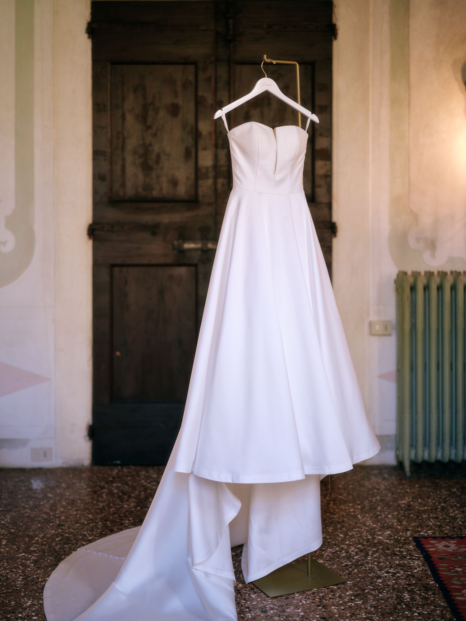 A series of five white wedding dresses hanging on display in a historic room with stone walls and wooden doors.
