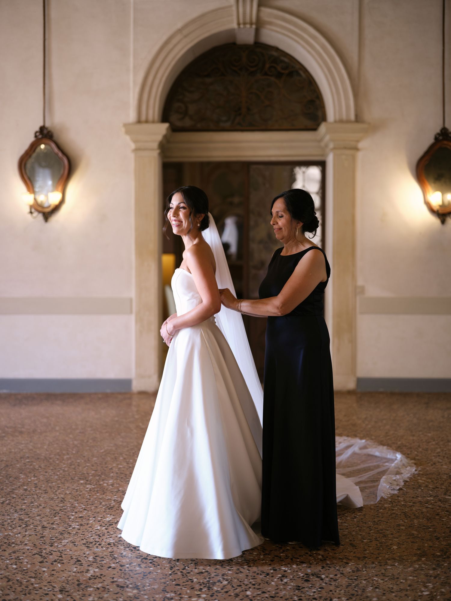 Two people embrace in a grand hallway with ornate architectural details and warm lighting.